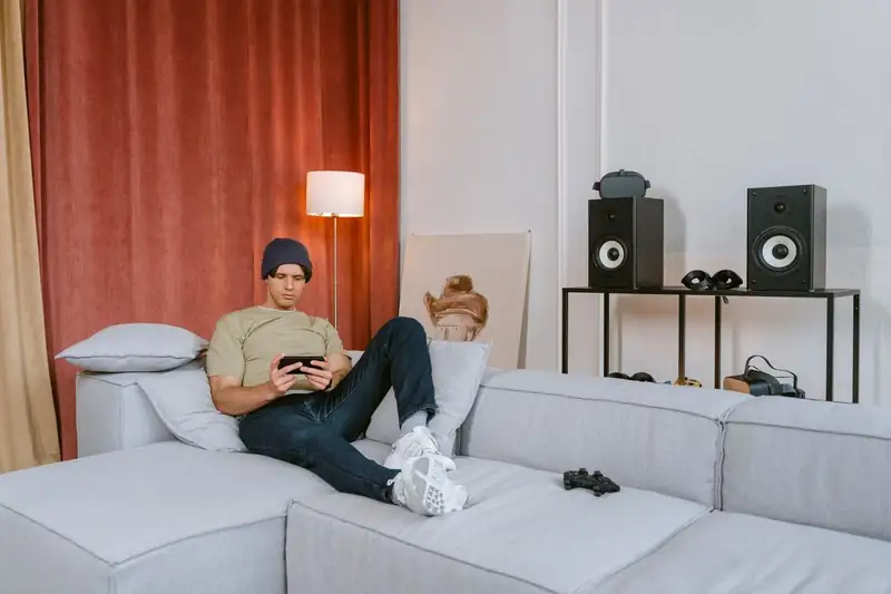 Young man playing a mobile game on a sofa – JLPUB fishing games on mobile